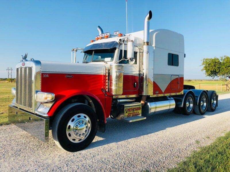 A red and white semi truck is parked on a gravel road