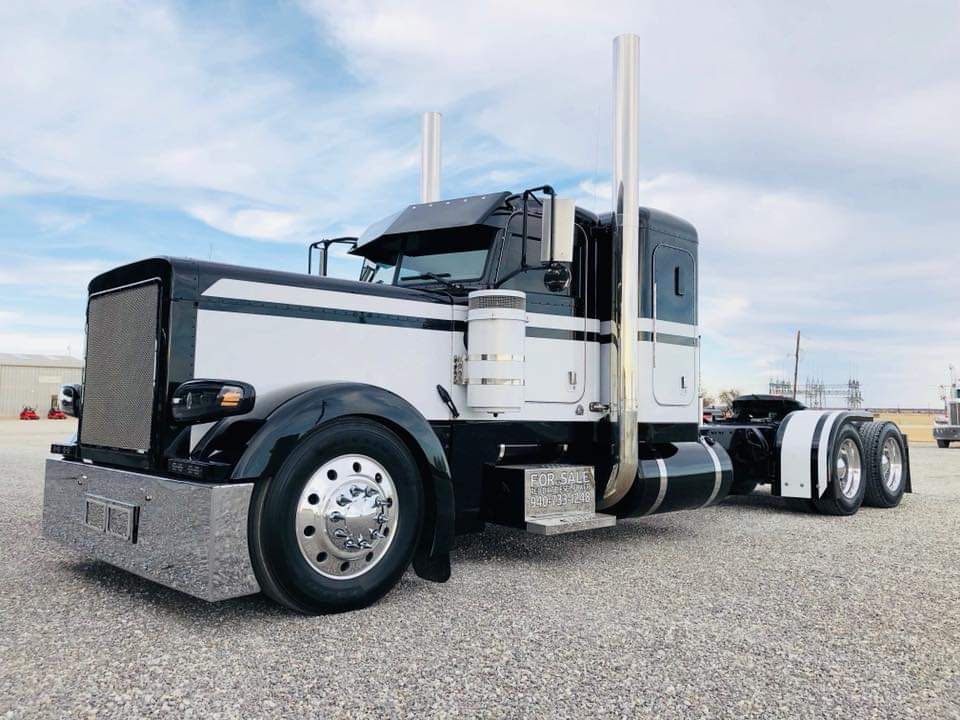 A black and white semi truck is parked in a gravel lot.