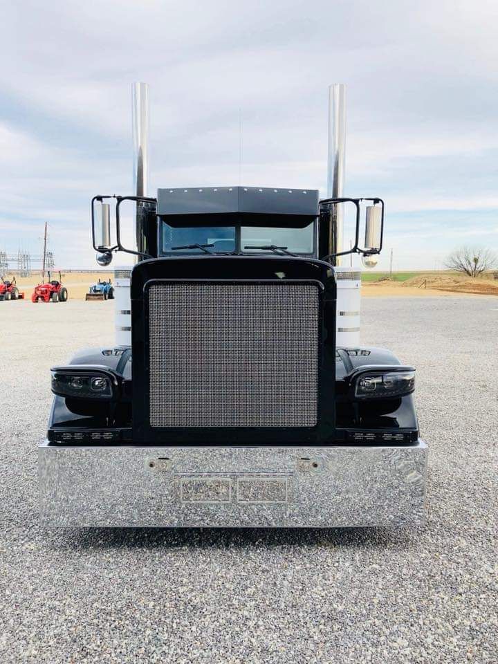 A black semi truck is parked in a gravel lot.