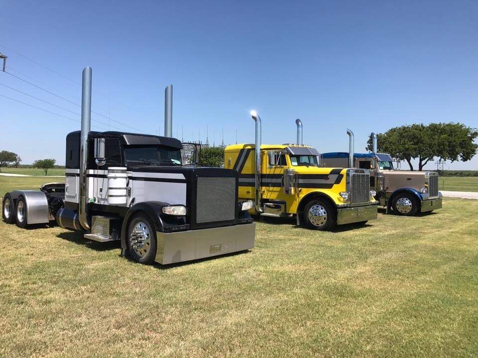 Three semi trucks are parked in a grassy field.
