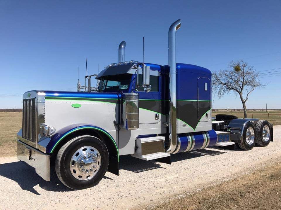 A blue and white semi truck is parked on the side of a dirt road.