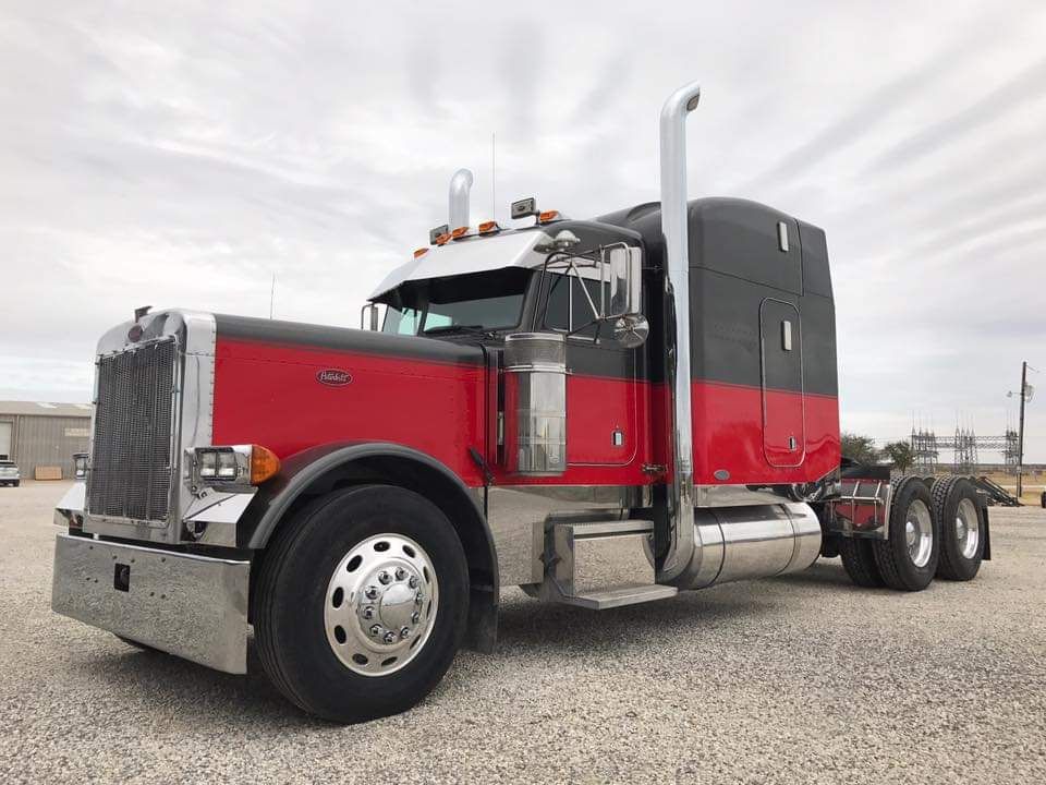 A red and black semi truck is parked in a gravel lot.