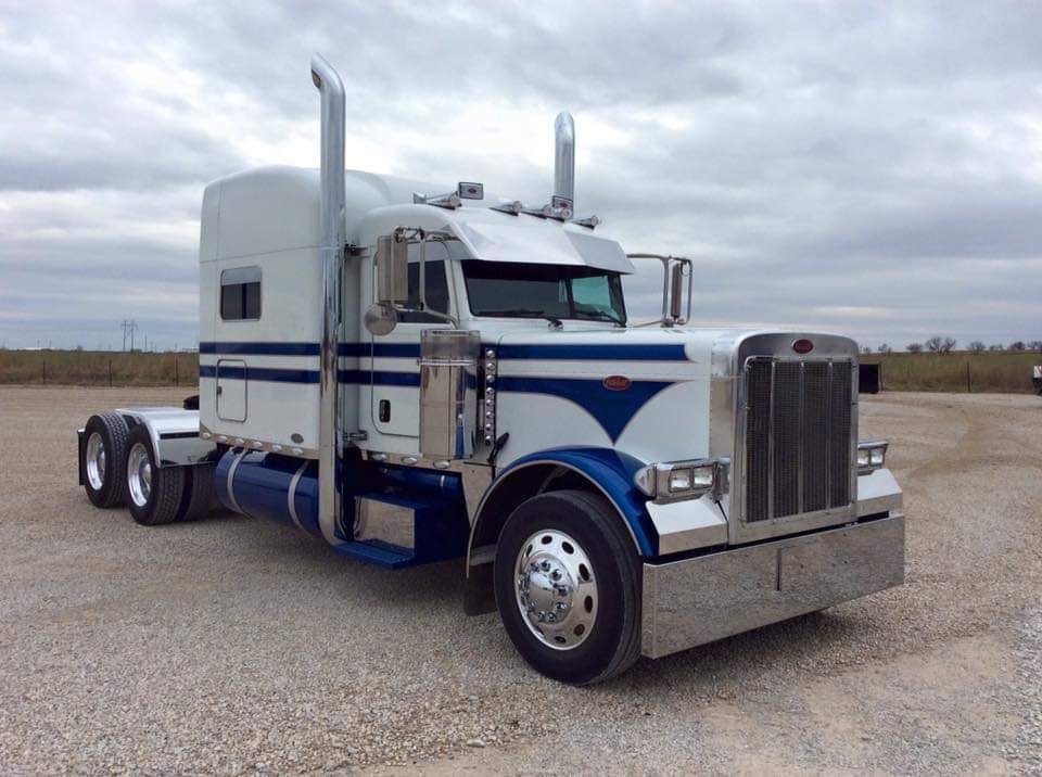 A white and blue semi truck is parked in a gravel lot.