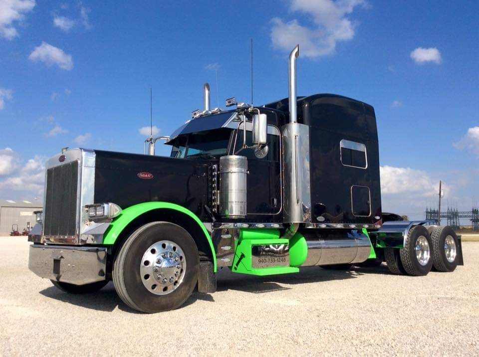 A black semi truck with green fenders is parked on a gravel road.
