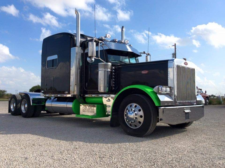 A black semi truck with green fenders is parked on the side of the road.