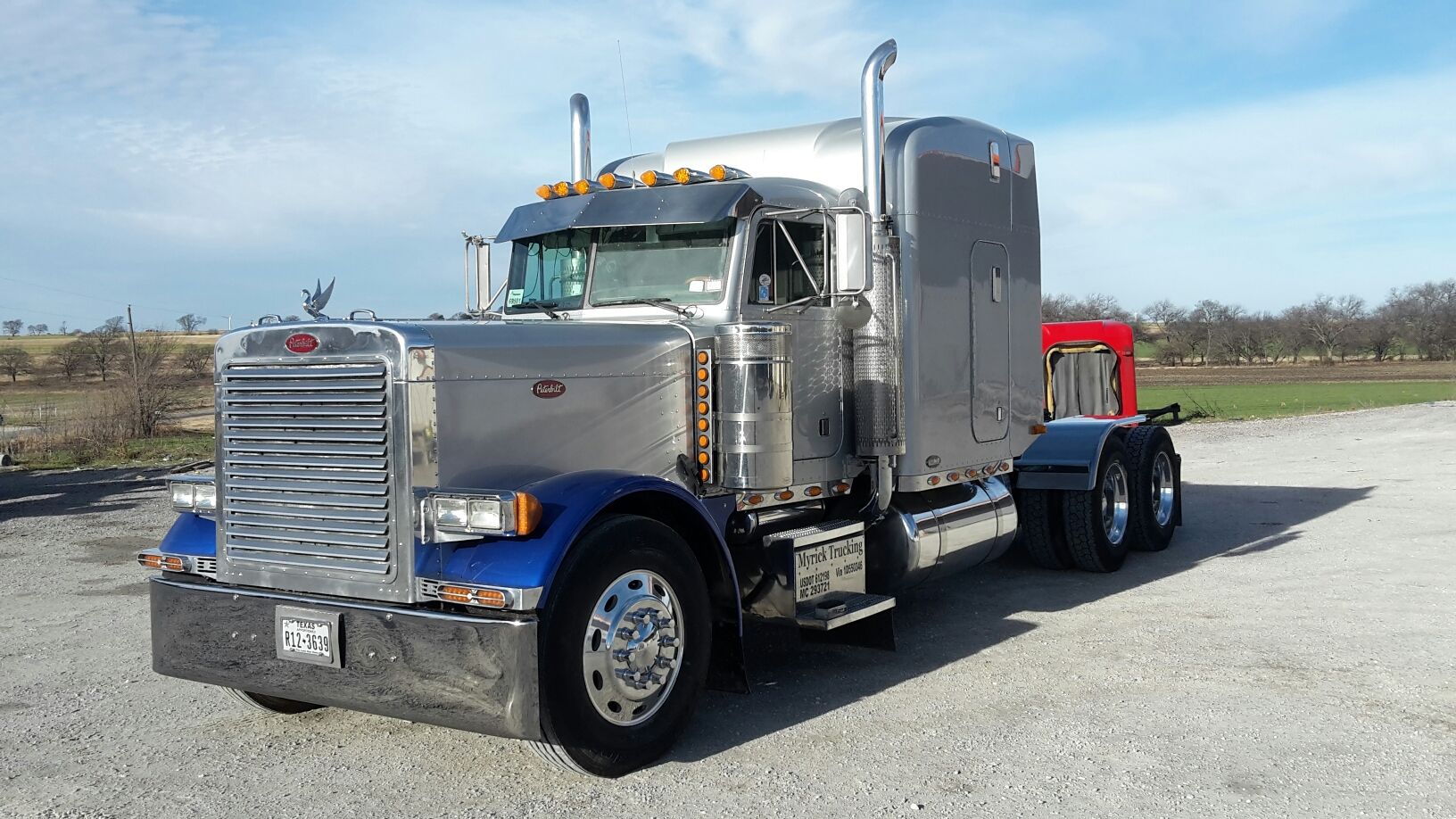 A silver semi truck is parked in a gravel lot.