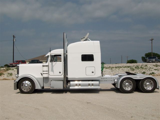 A white semi truck is parked on a dirt road