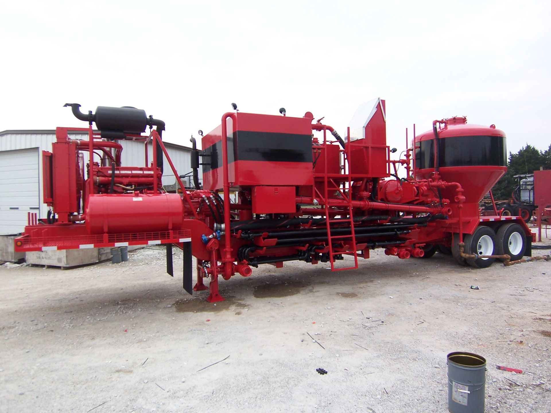 A large red machine is parked in a gravel lot