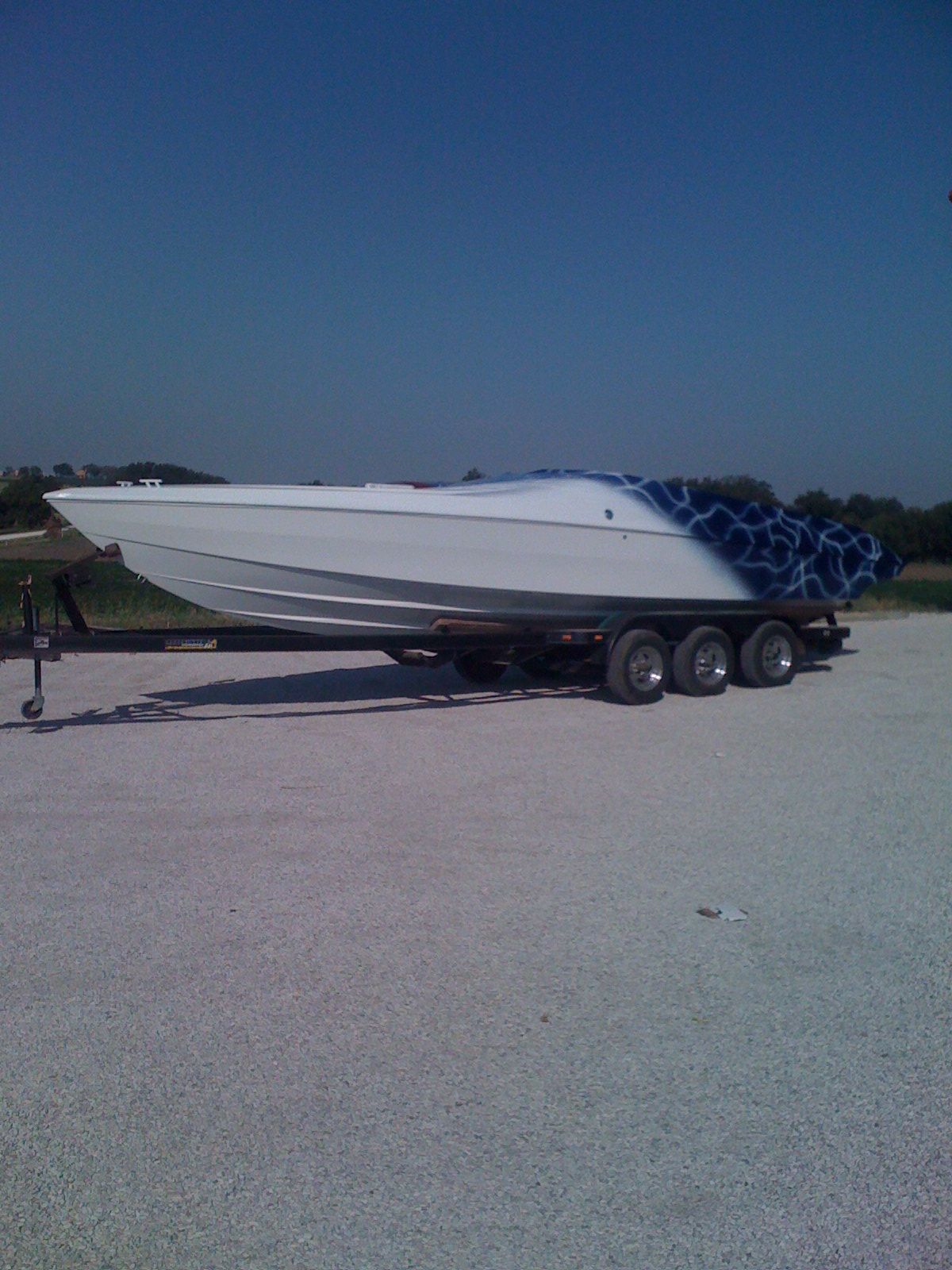 A white boat is on a trailer in a gravel lot