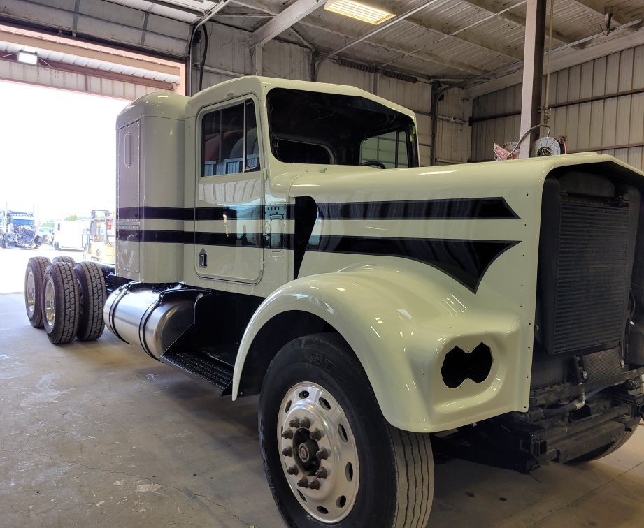 A white semi truck with black stripes is parked in a garage