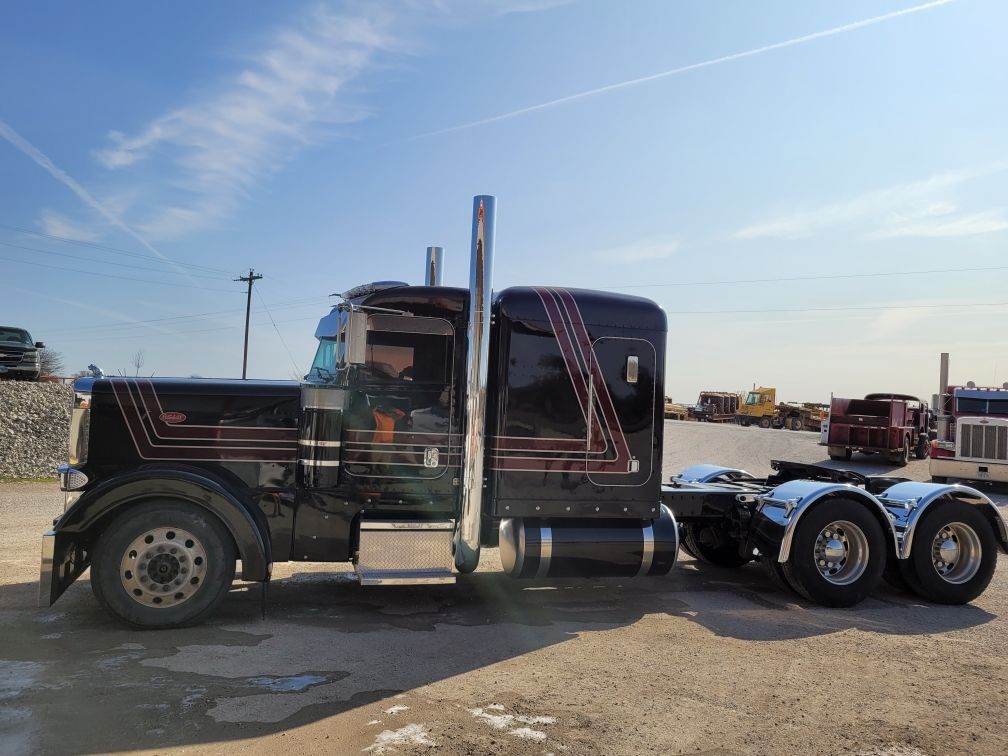 A black semi truck with a trailer is parked in a parking lot.