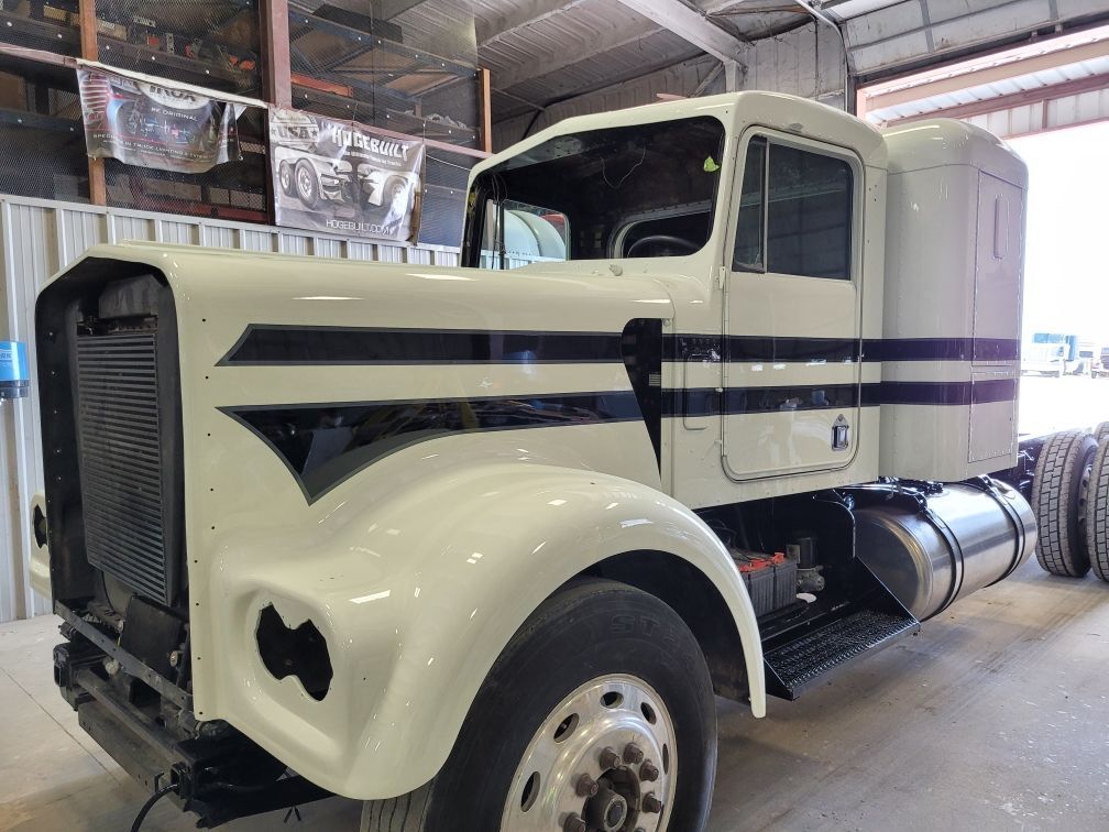 A white semi truck with black stripes on the side is parked in a garage.