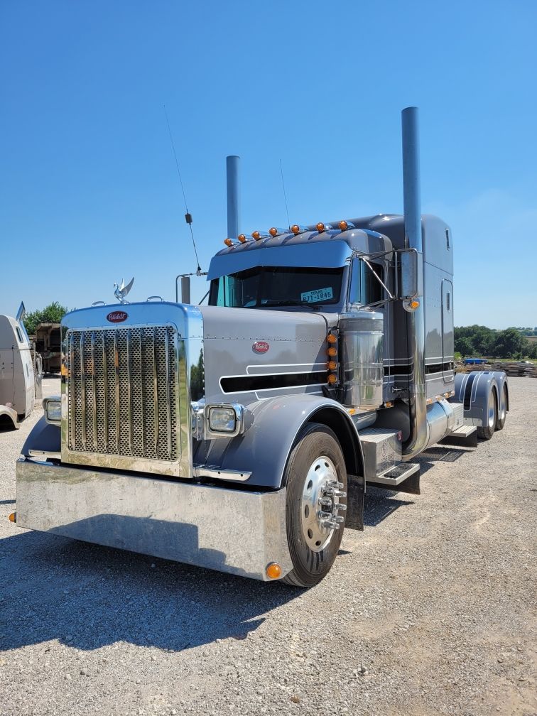 A silver semi truck is parked in a gravel lot on a sunny day.