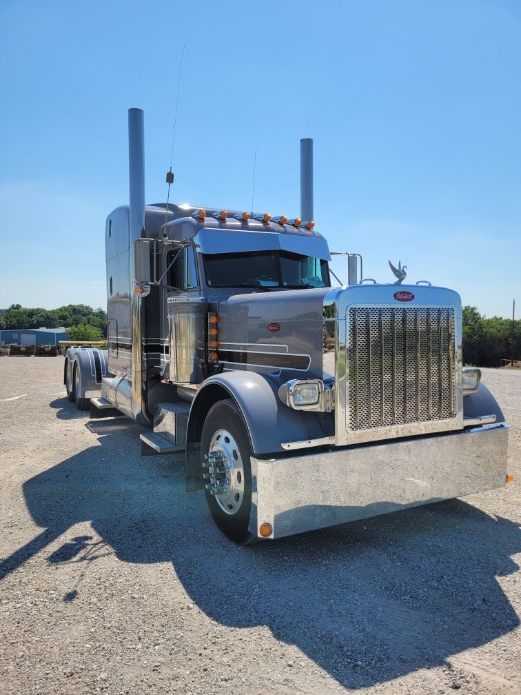 A silver semi truck is parked in a parking lot on a sunny day.