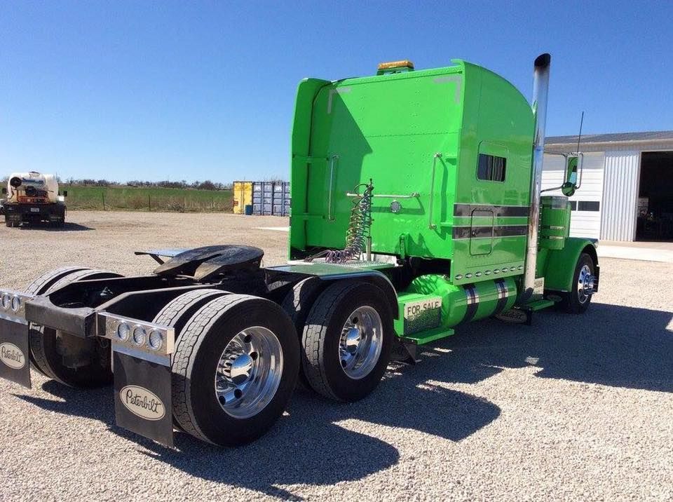 A green semi truck is parked in a gravel lot