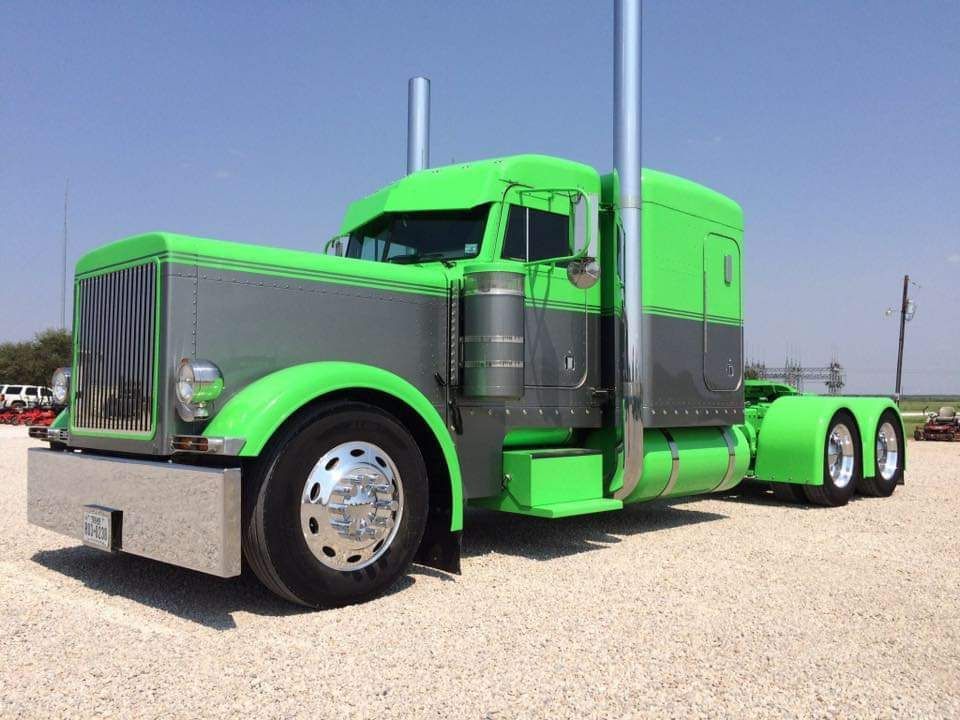 A green semi truck is parked in a gravel lot