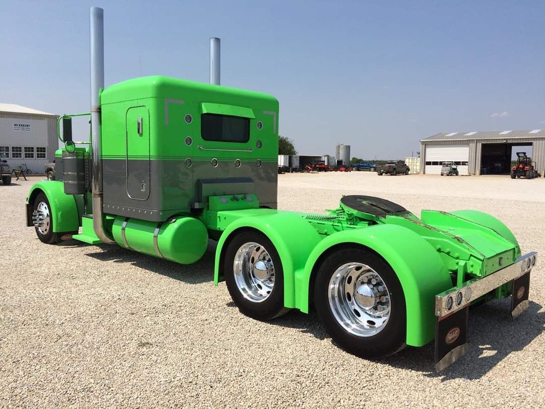 A green semi truck is parked in a gravel lot.