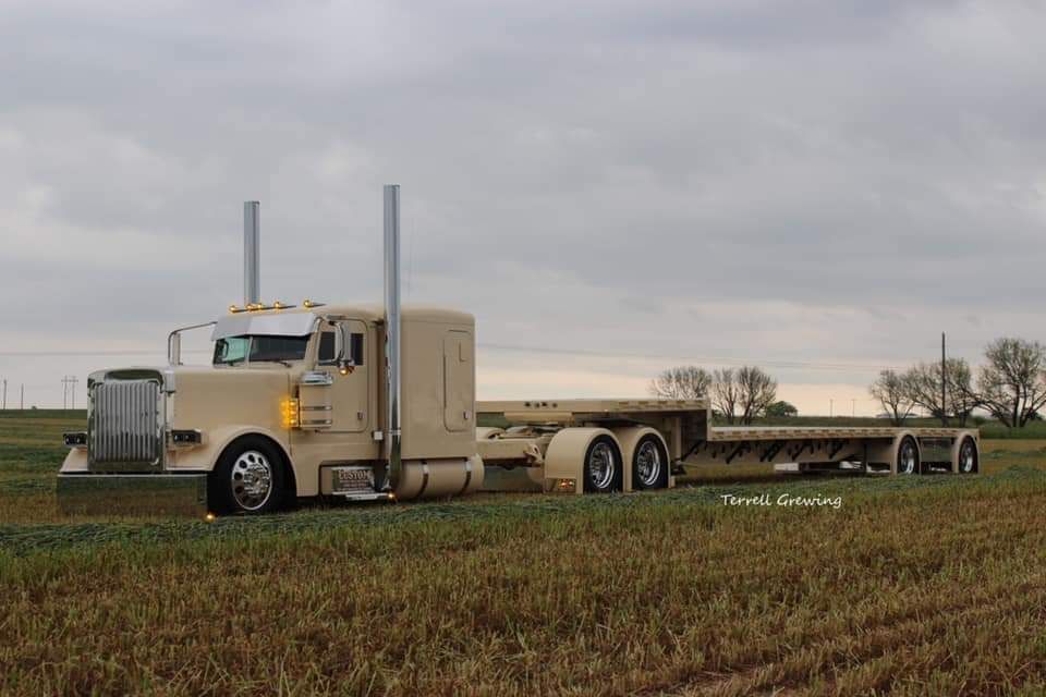A semi truck with a flatbed trailer is parked in a field.