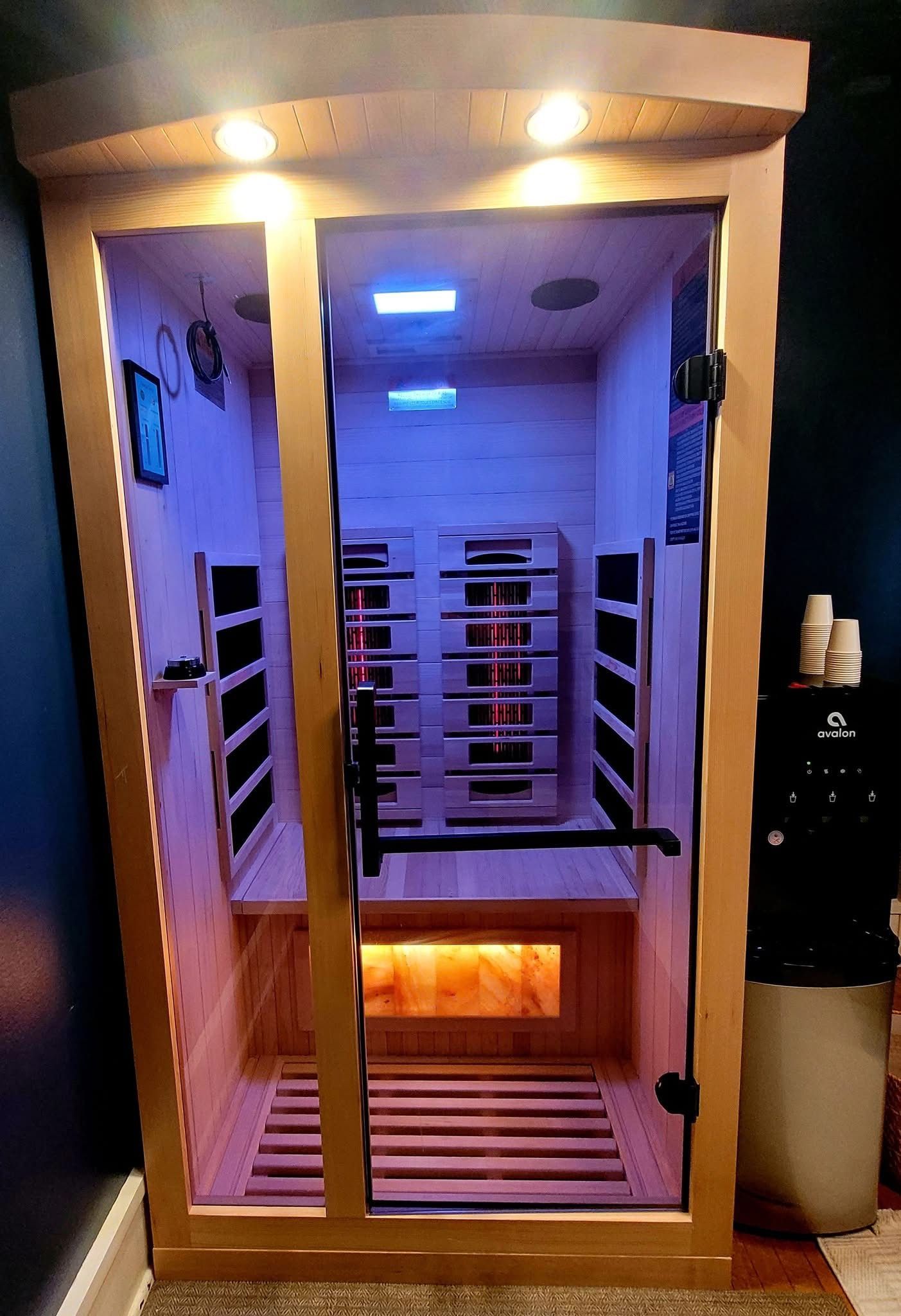 A wooden, glass-door sauna with interior ambient lighting, heating panels, and a salt block feature.