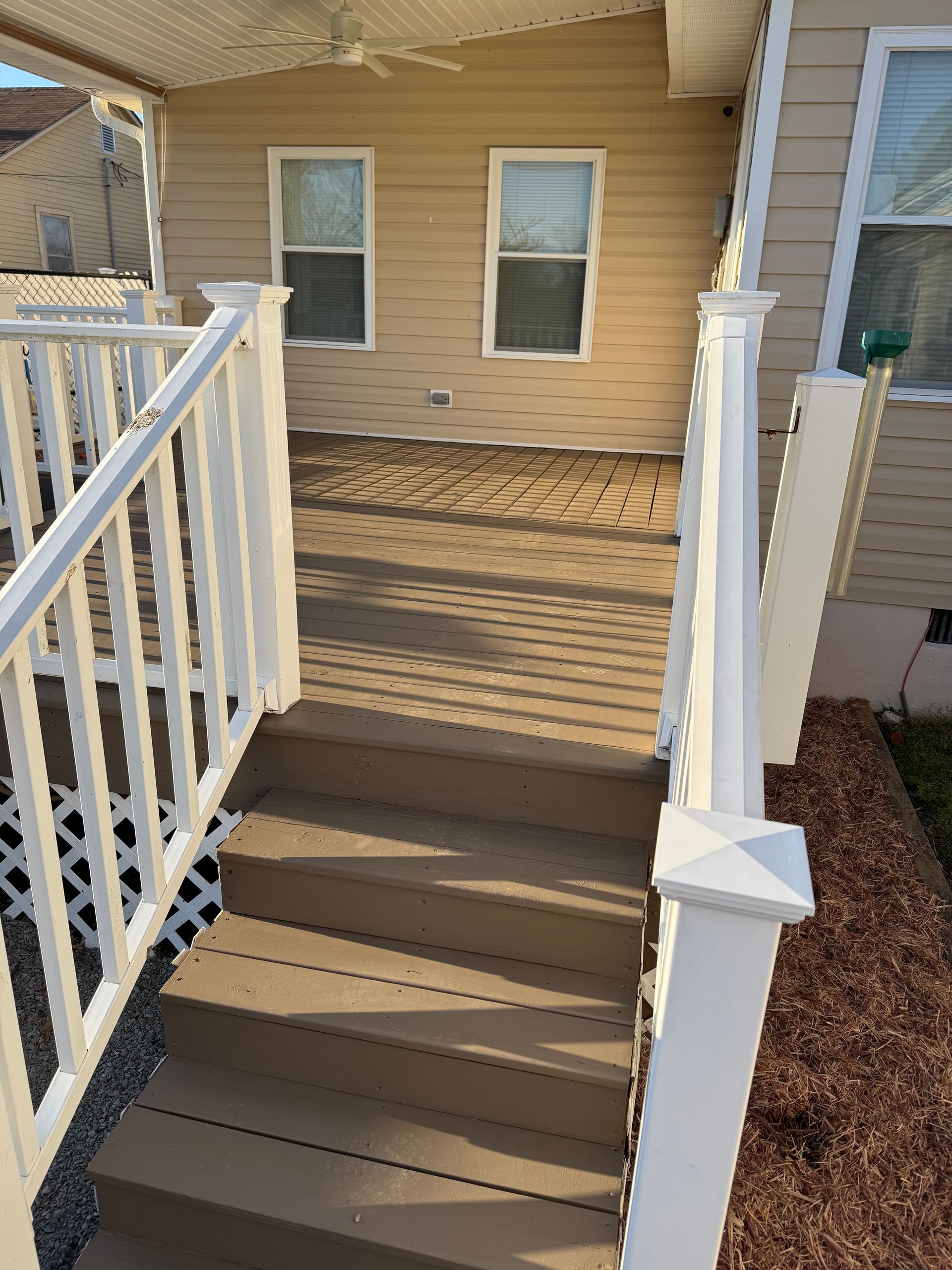 Deck with steps, white railing, leading to a house with two windows