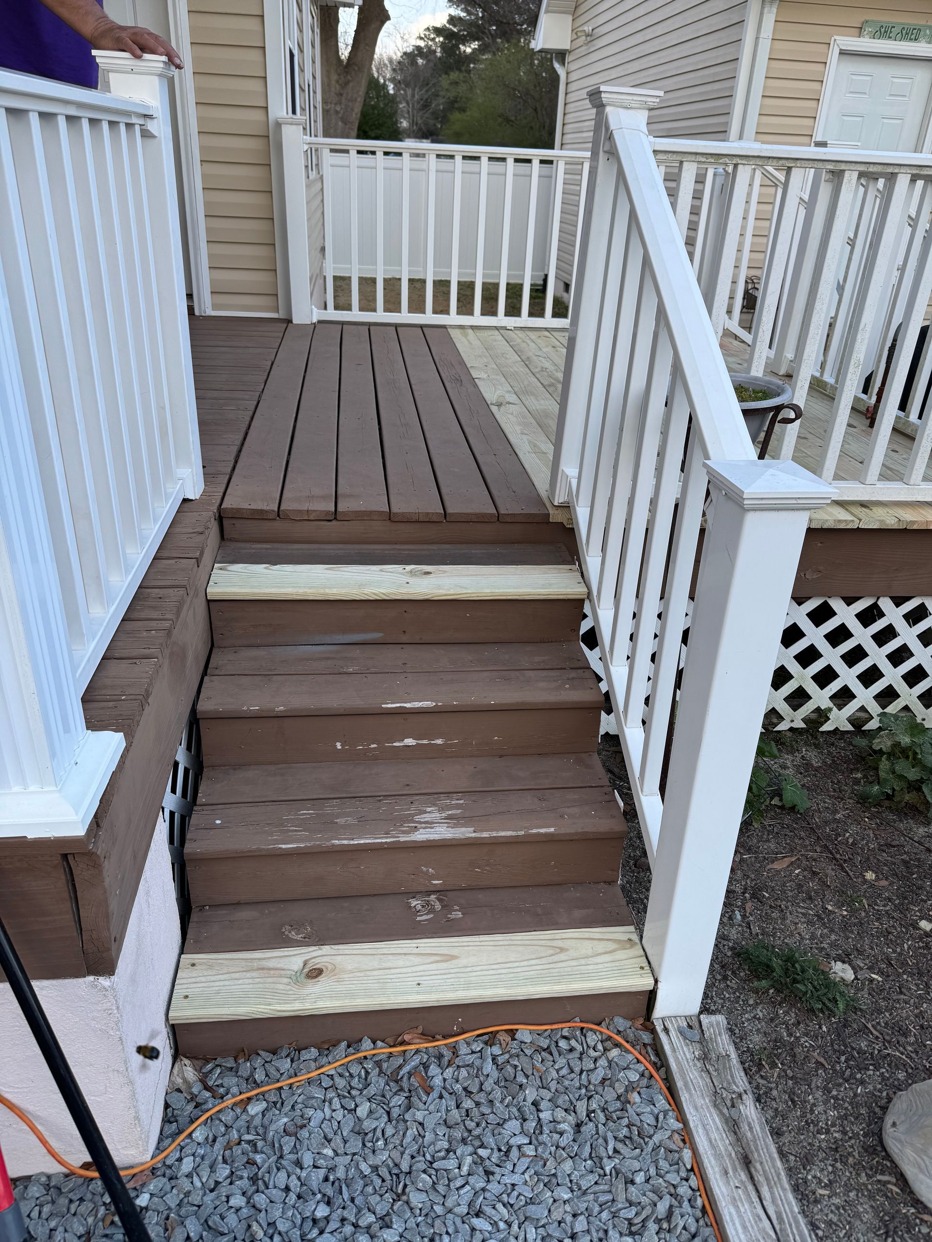 Wooden deck with stairs; brown steps, white railing, and pebble ground