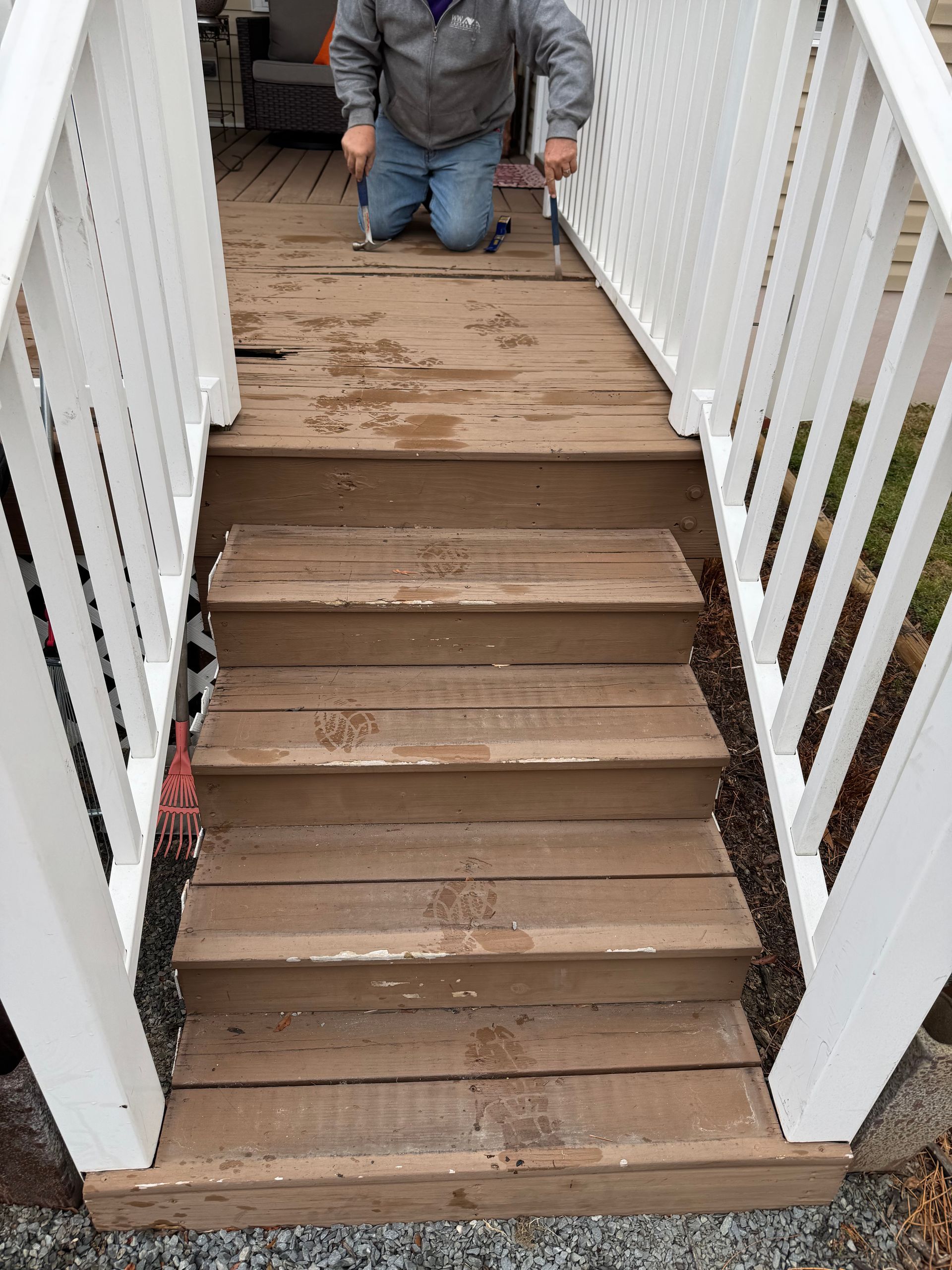 Wooden deck stairs with a person kneeling on the deck above. White railing on both sides of the stairs