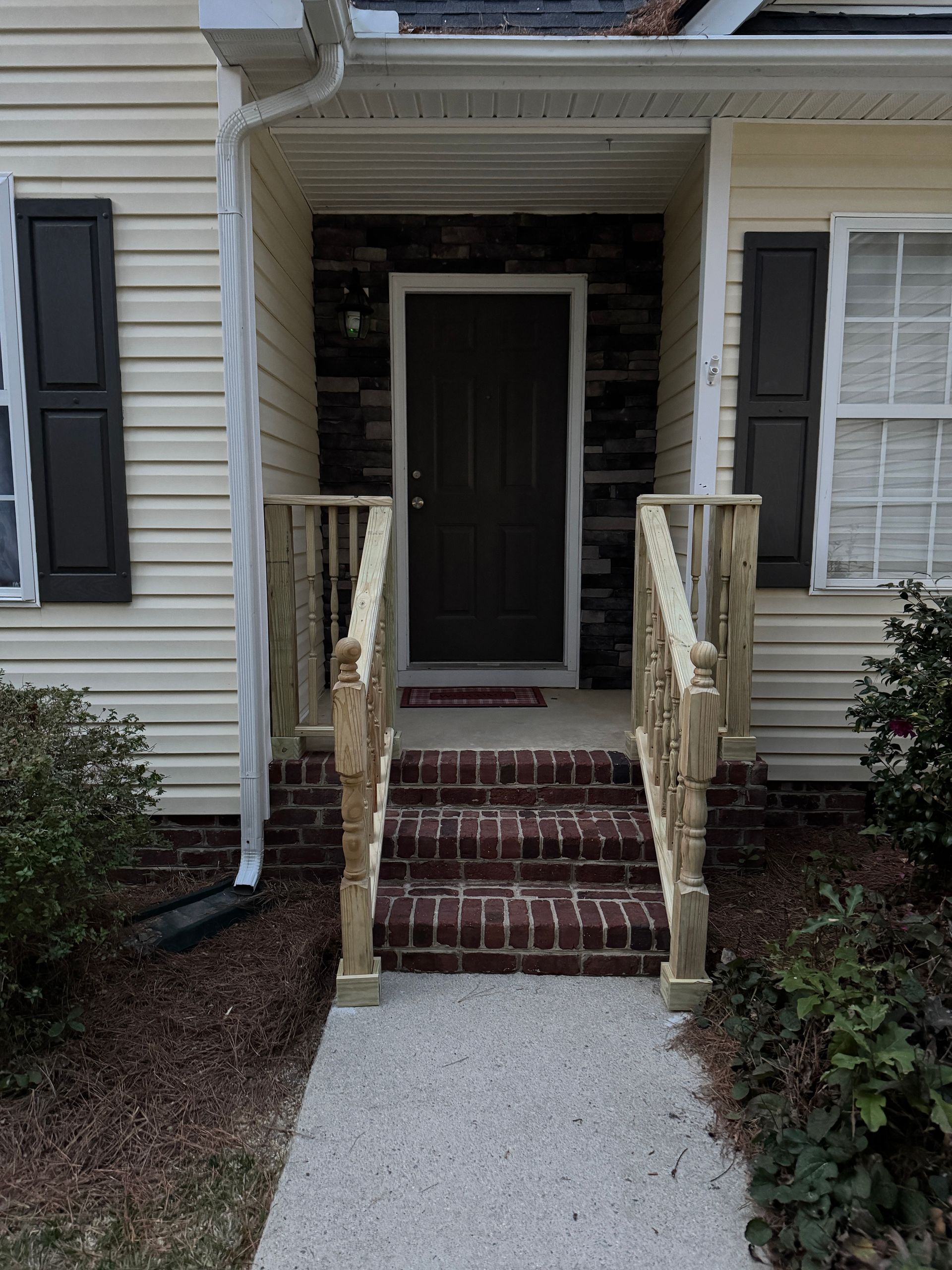 Entrance to a house with steps, a brown door, and wooden railing