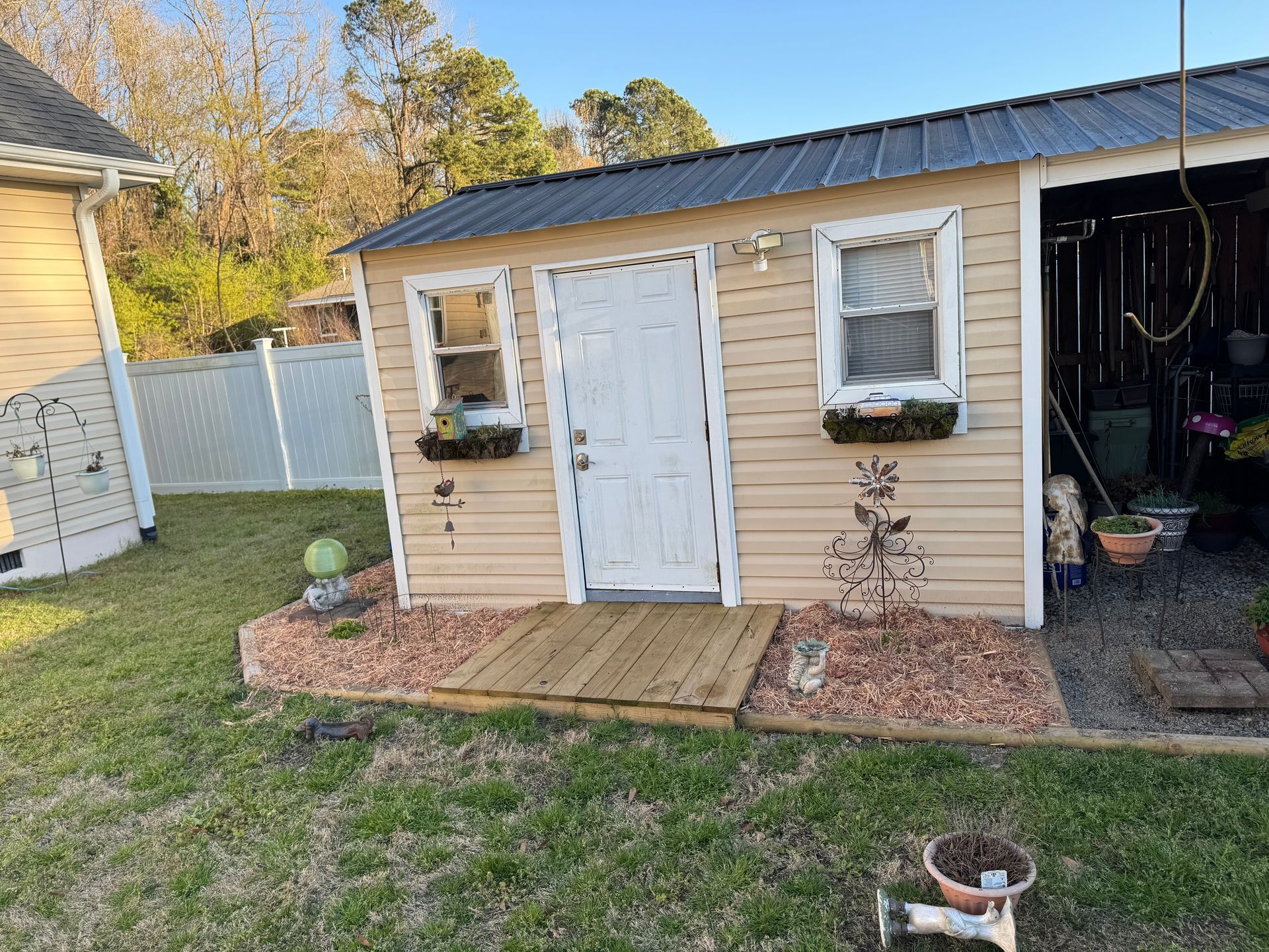 Tan shed with a black roof, white door, and flower boxes