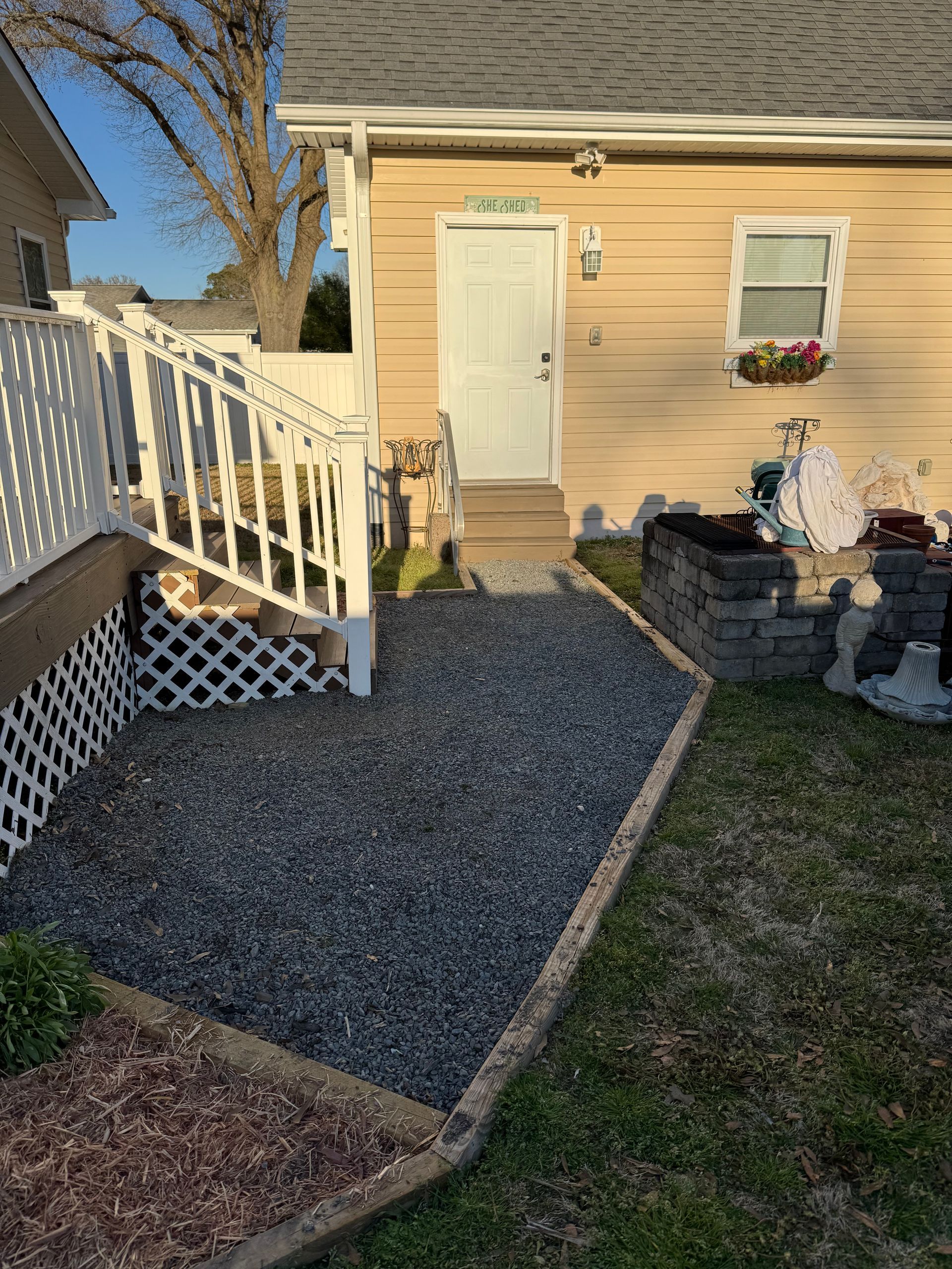 Gravel path leading to a white door with stairs and a small window, edged by a low wall and lawn