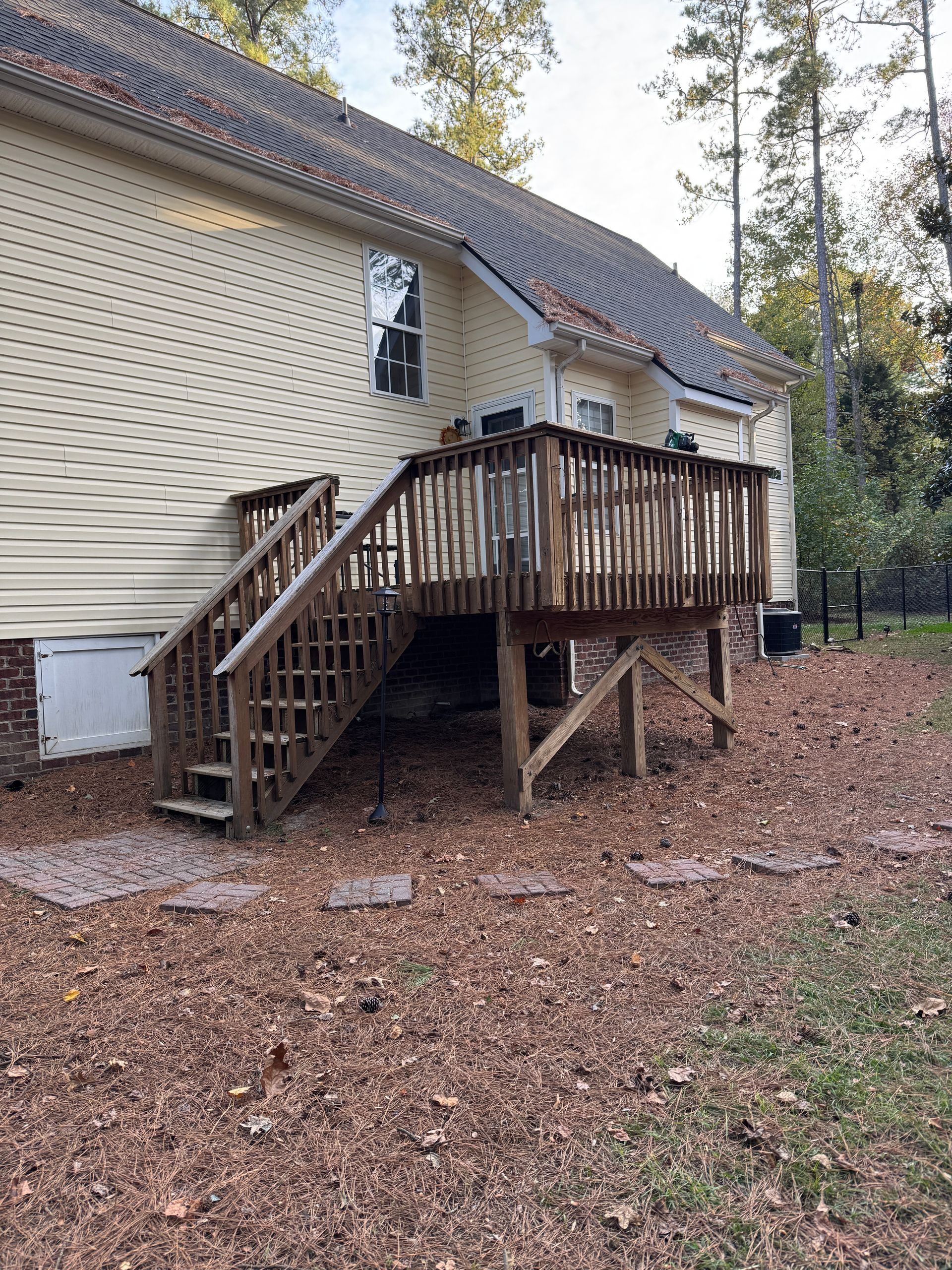 Wooden deck with stairs attached to a yellow house, set in a yard covered in brown mulch