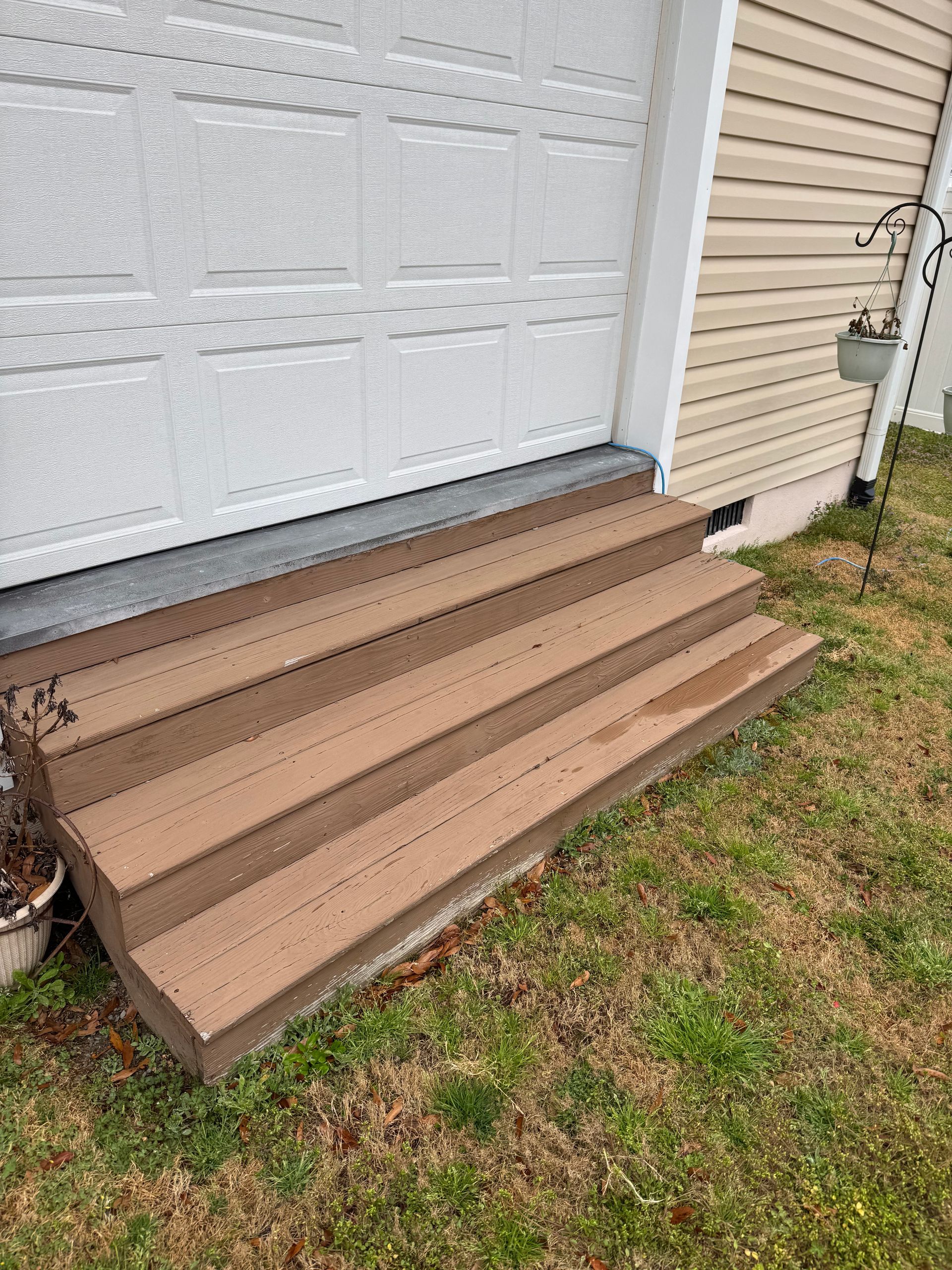 Brown composite steps leading up to a white garage door, set on a patch of grass