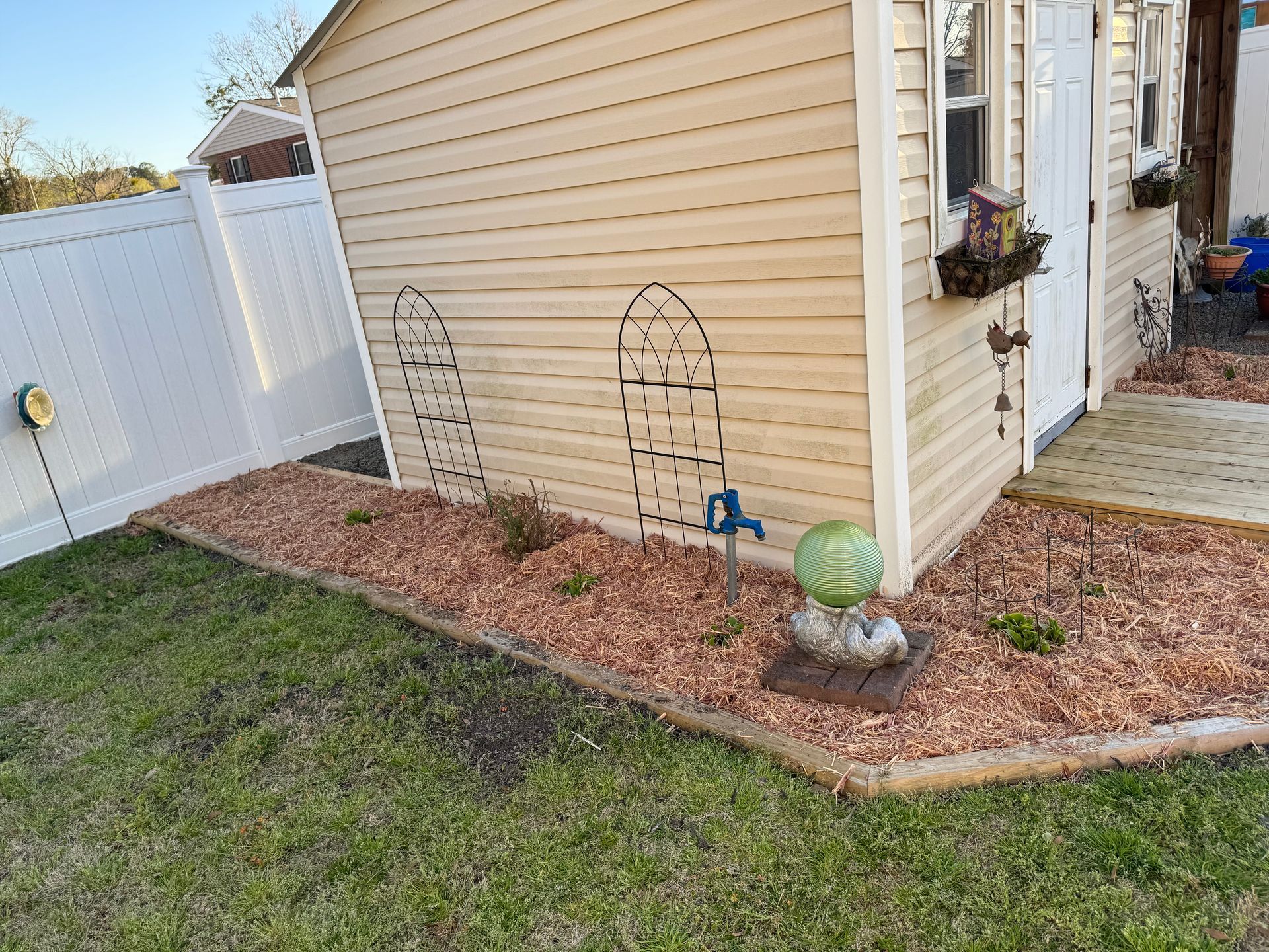Tan shed with flower beds, white fence, and green grass