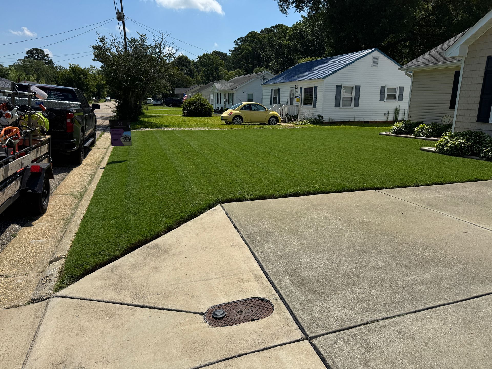 A freshly cut green lawn in front of a white house with a blue roof