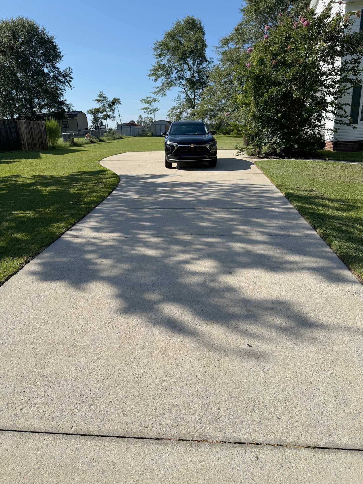 SUV parked on a concrete driveway, casting shadows, bordered by green grass and trees