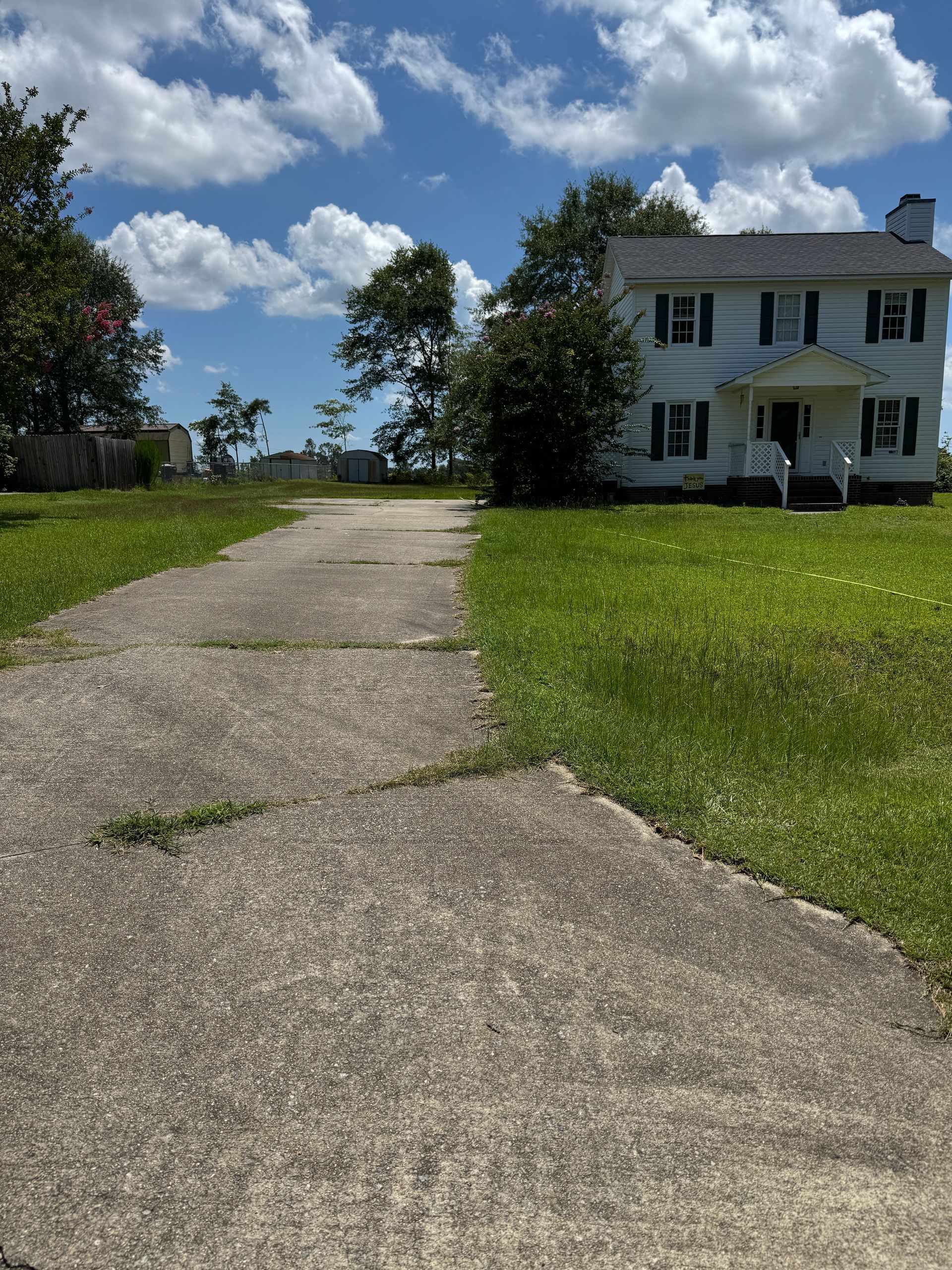 Concrete driveway leading to a two-story white house with green shutters