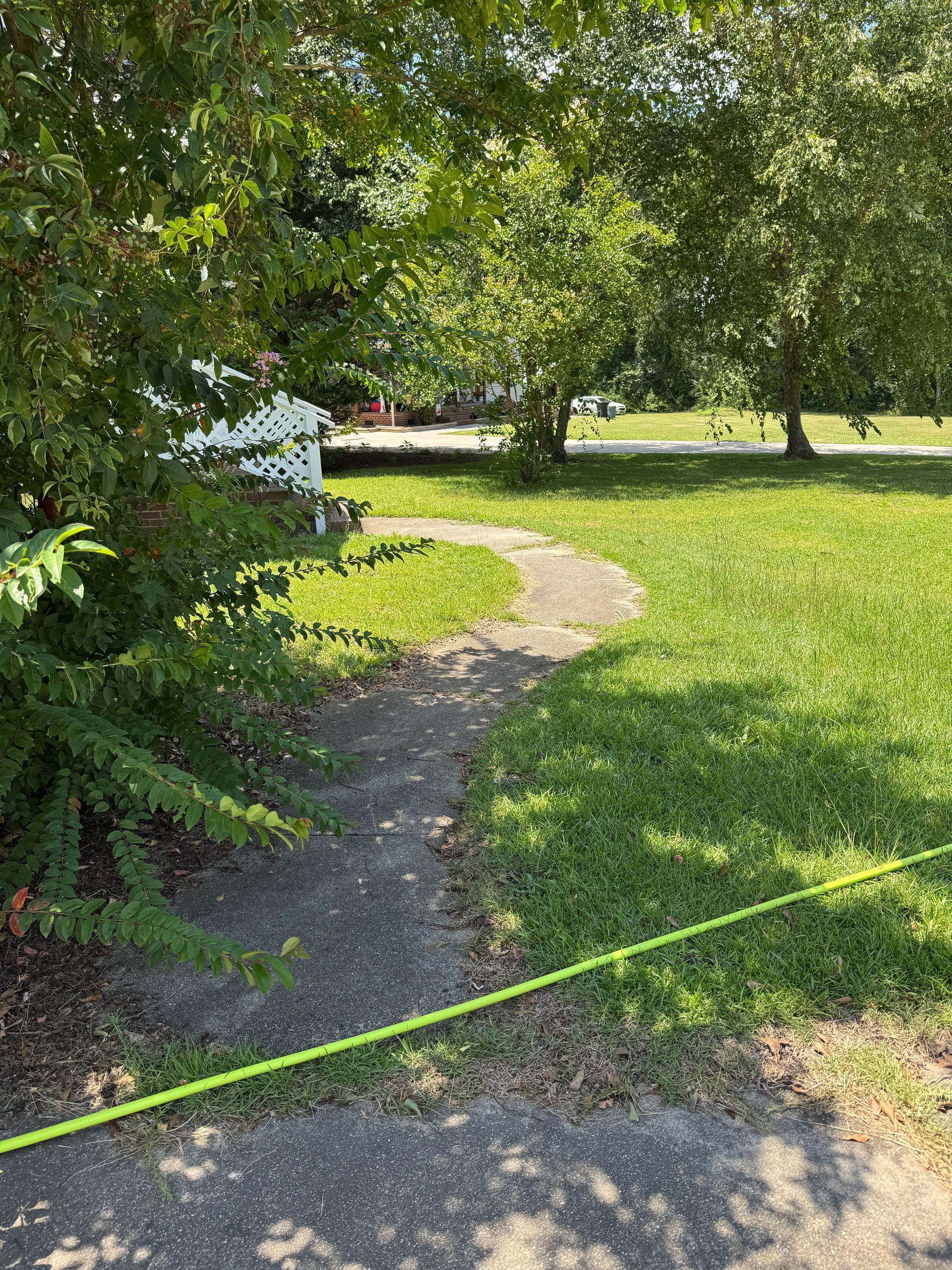Curved concrete path through a grassy yard, leading to a small building under trees