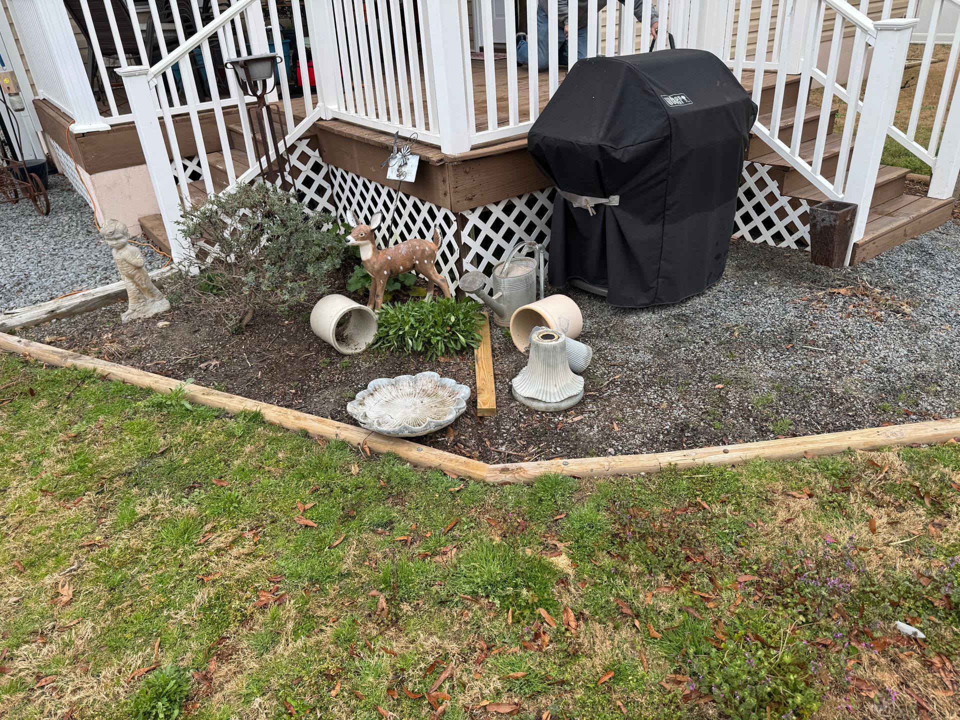 A small garden bed with a deer statue, planters, and a covered grill next to a white porch