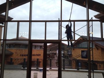 Person washing windows inside a building with a scaffolding; buildings with storefronts are visible outside.