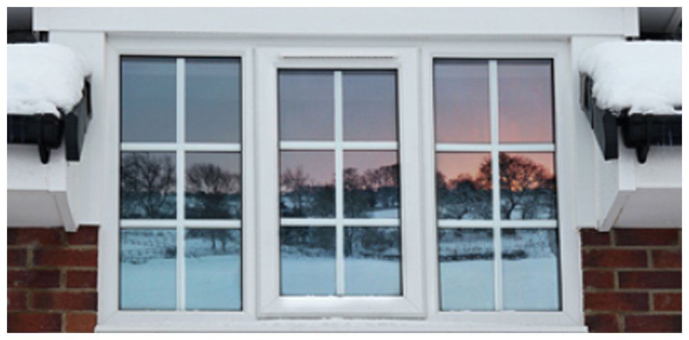 Three white-framed windows reflect a snowy landscape and a colorful sunset. Snow rests on the roof overhang.