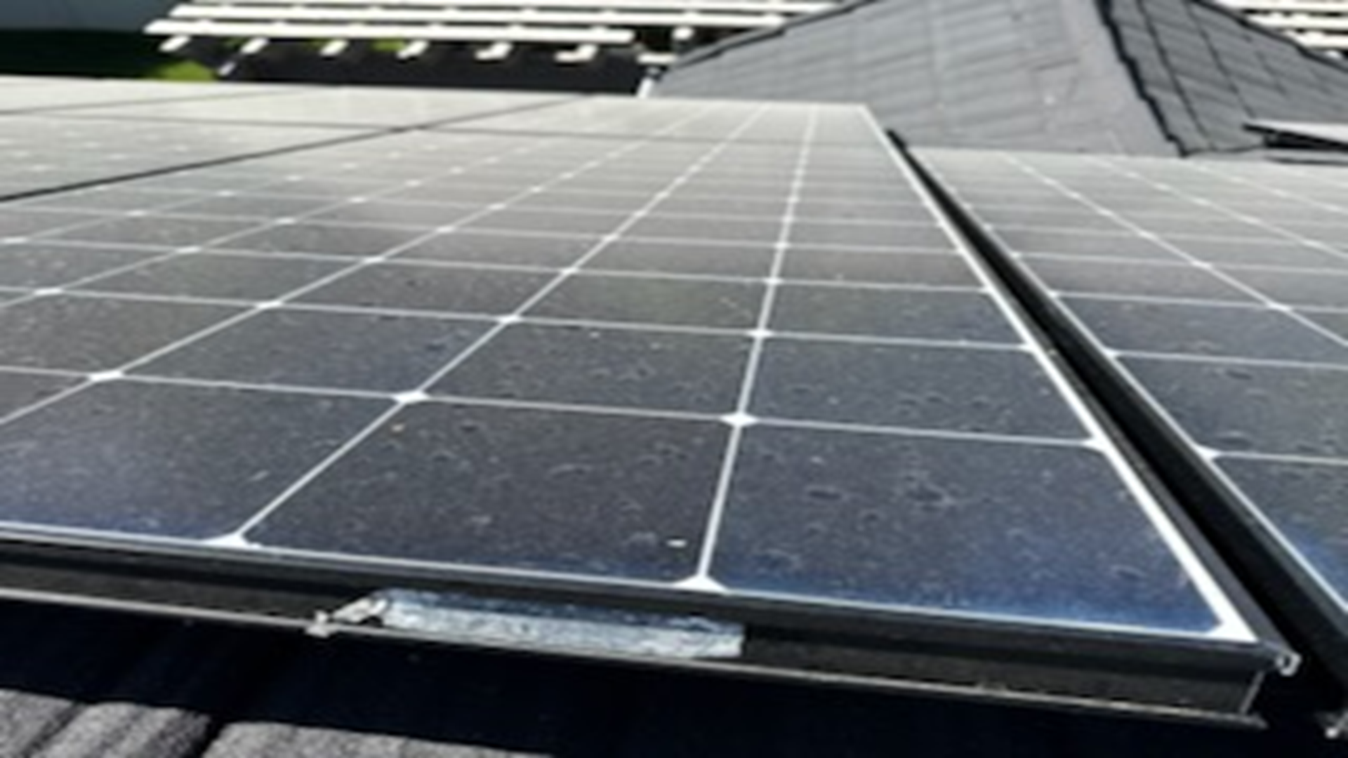 Solar panels on a roof, covered in dust, with black frames and a gray rooftop in the background.