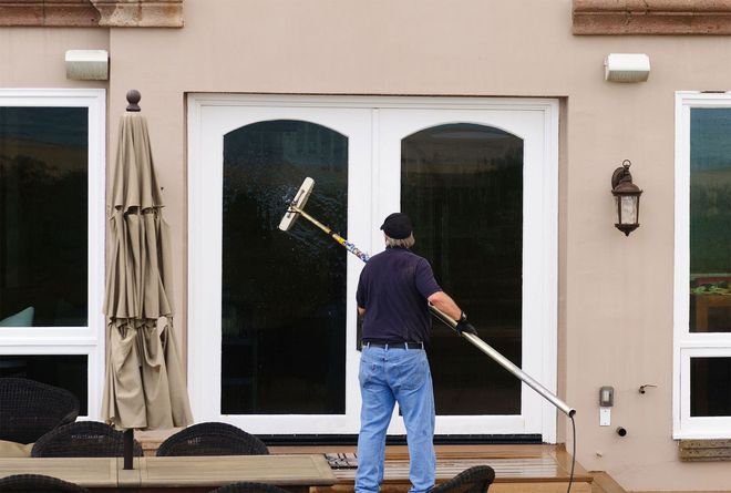 Person cleaning a large glass door with a long-handled squeegee, outdoors.