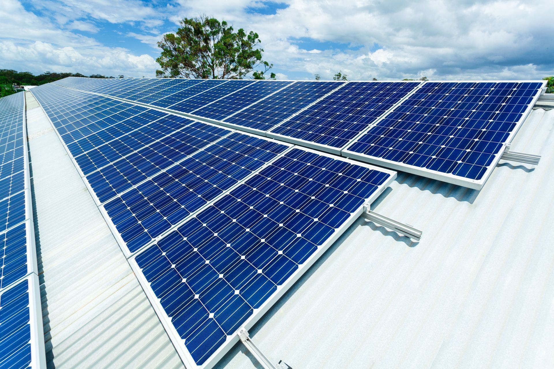 Solar panels on a metal roof, capturing sunlight. Blue panels against a partly cloudy sky.