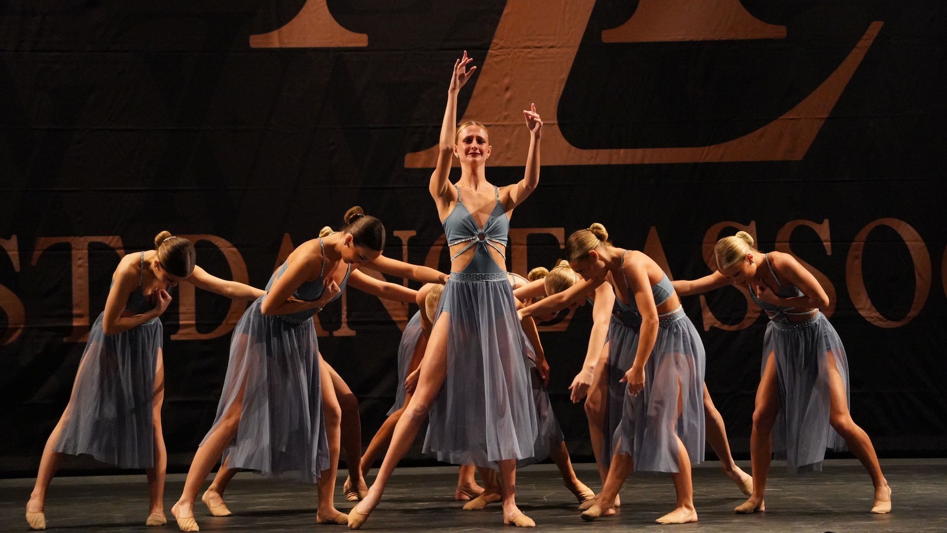 A group of women are dancing on a stage in front of a sign that says imagine