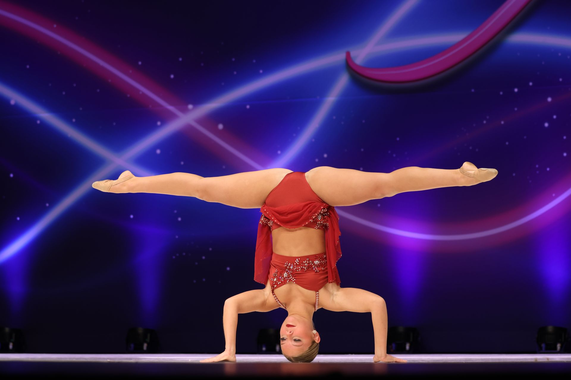 A gymnast is doing a handstand on a red background