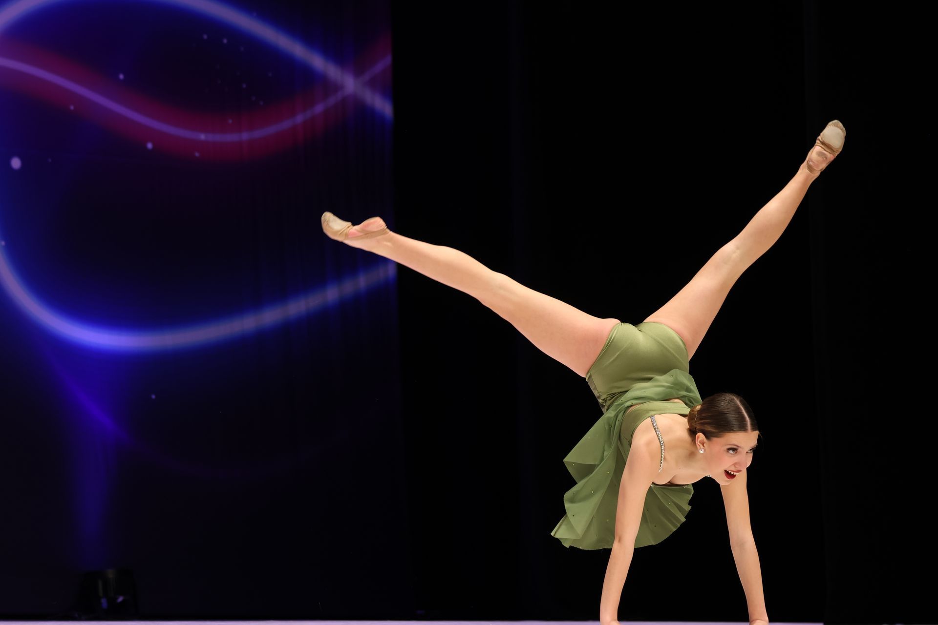 A young girl in a pink dress is doing a handstand on the floor