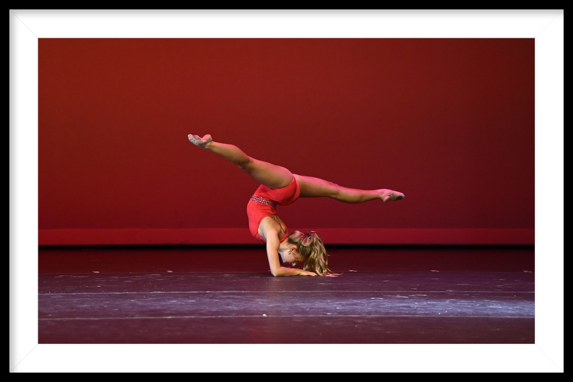 A young girl in a pink dress is doing a handstand on the floor