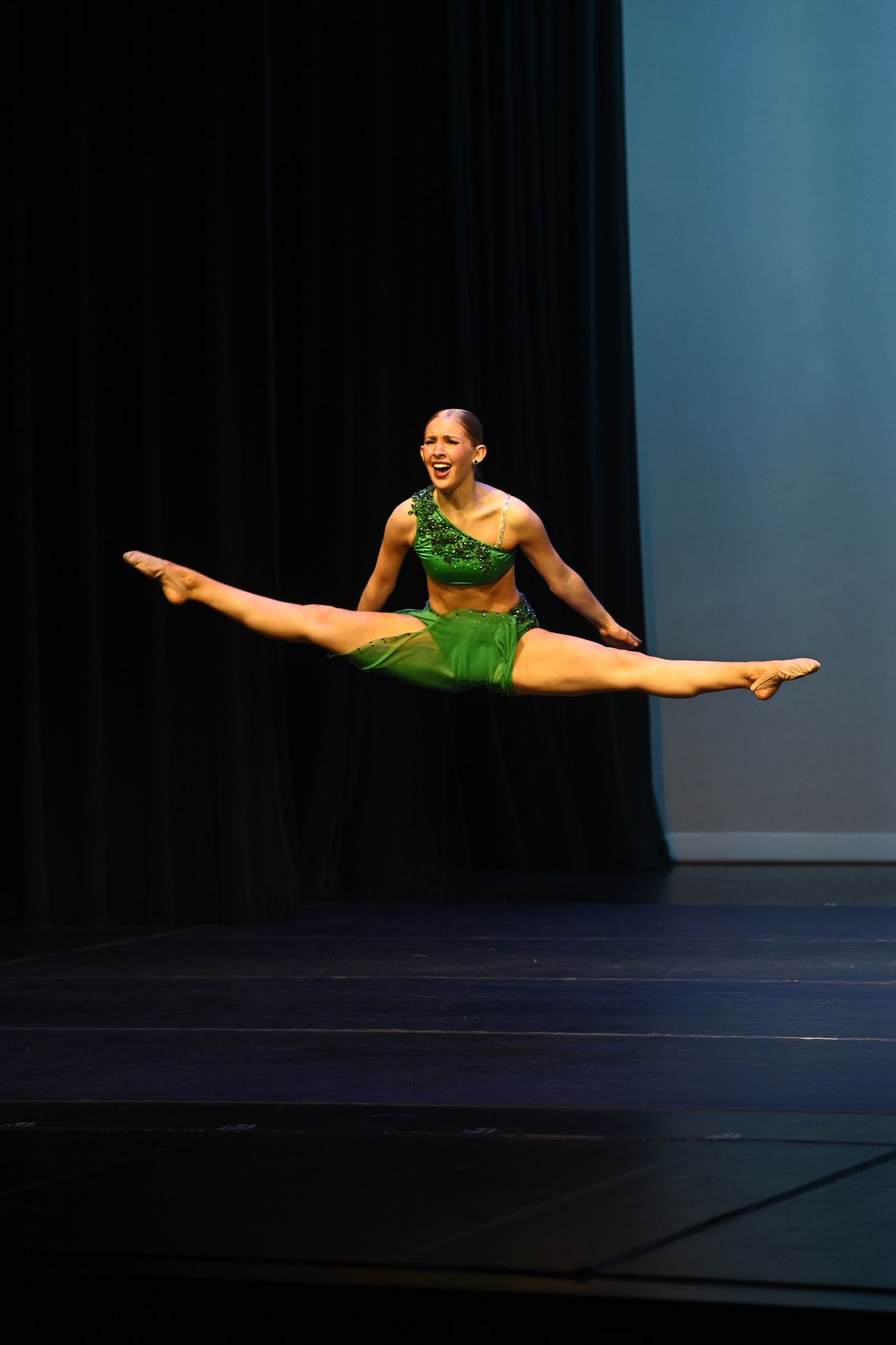 A woman is sitting on the floor on a stage with her arm in the air.
