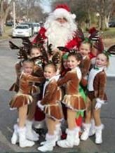 A group of young girls in reindeer costumes are posing for a picture with santa claus.