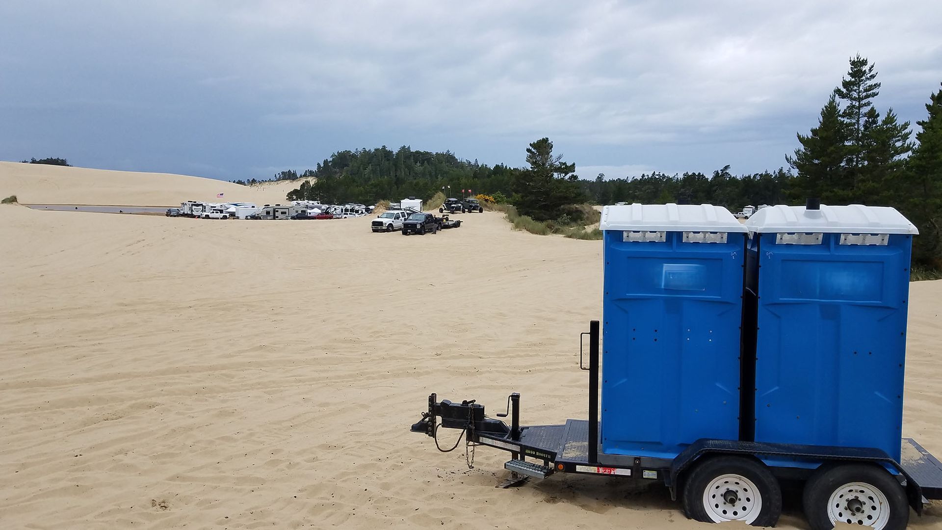Two blue portable toilets are on a trailer in the sand.