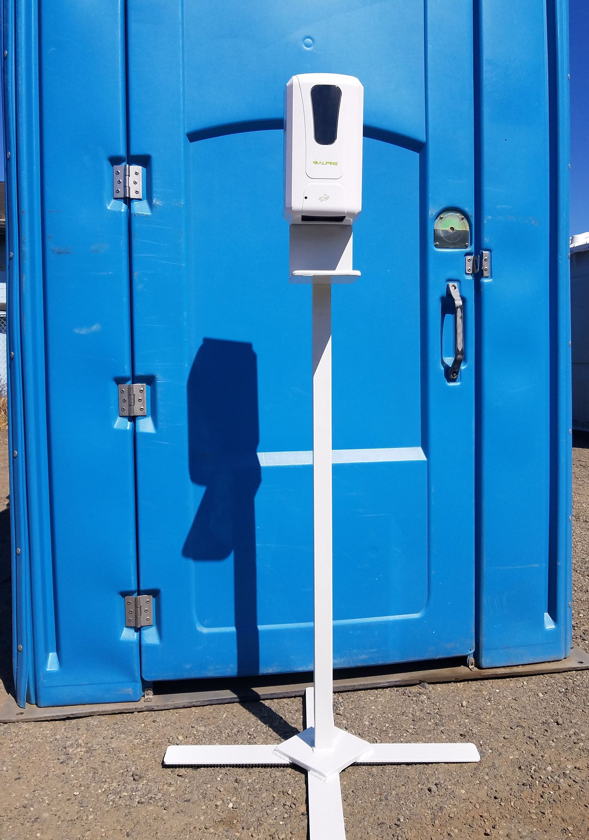 A hand sanitizer dispenser is sitting in front of a blue toilet.